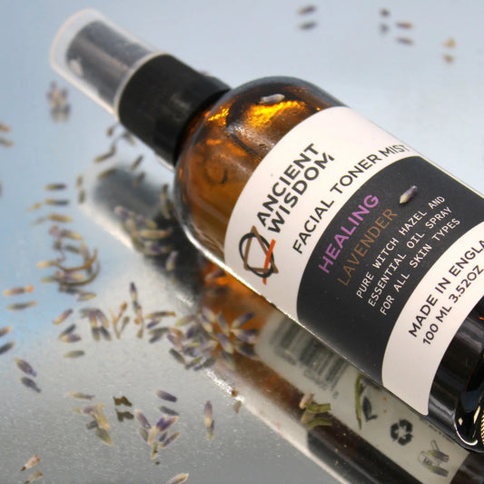 Frasco de vidrio ámbar con atomizador para tónico facial de lavanda, rodeado de flores secas sobre superficie brillante.
