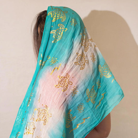 Bufanda de gasa azul turquesa con estampado dorado de tortugas y diseño degradado. Ideal para un look veraniego.