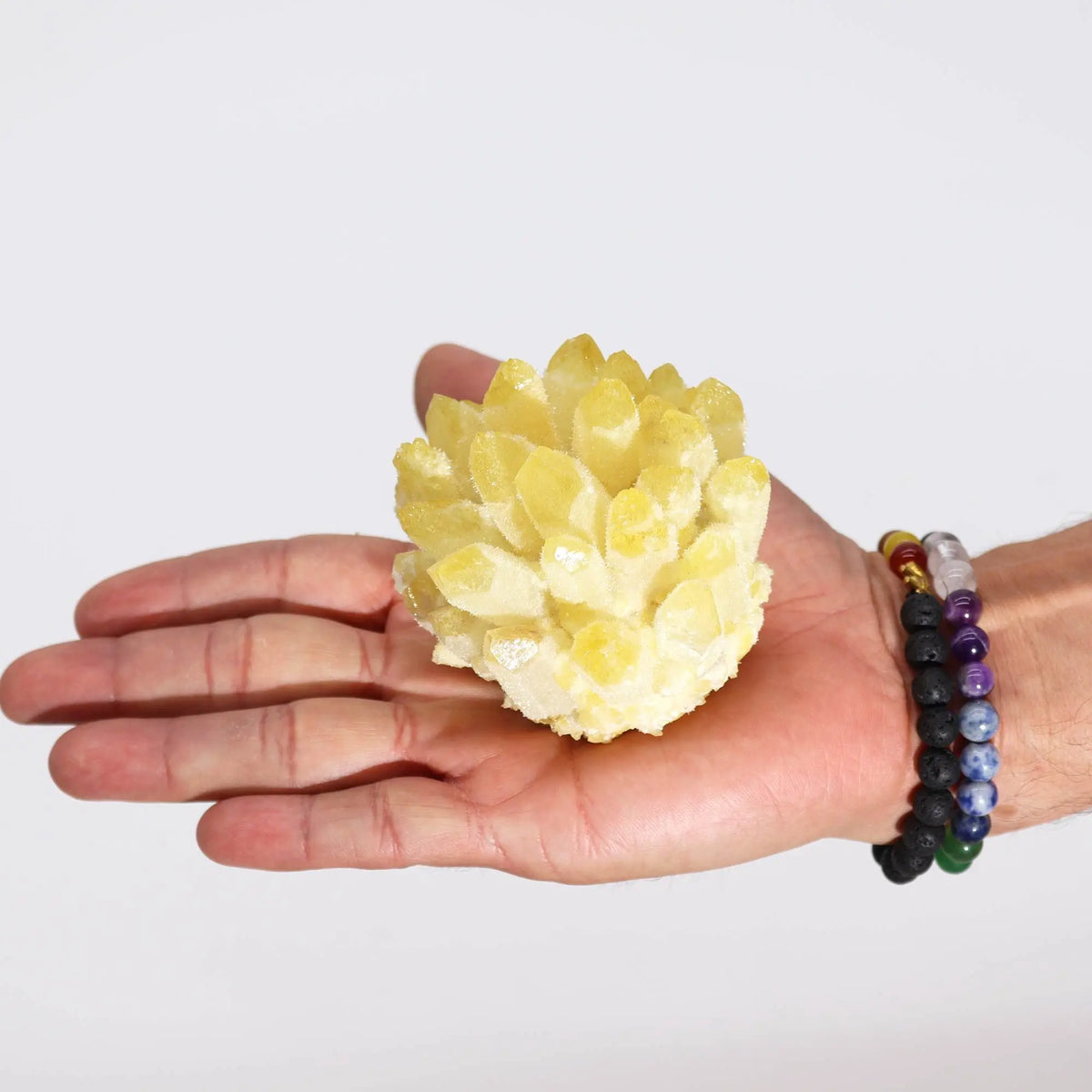 Racimo de cuarzo amarillo brillante con puntas cristalinas sostenido en la palma de una mano sobre fondo blanco.