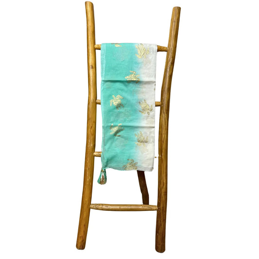 Pareo de algodón blanco y turquesa con estampado de tortugas doradas, colgado en una escalera decorativa de madera.