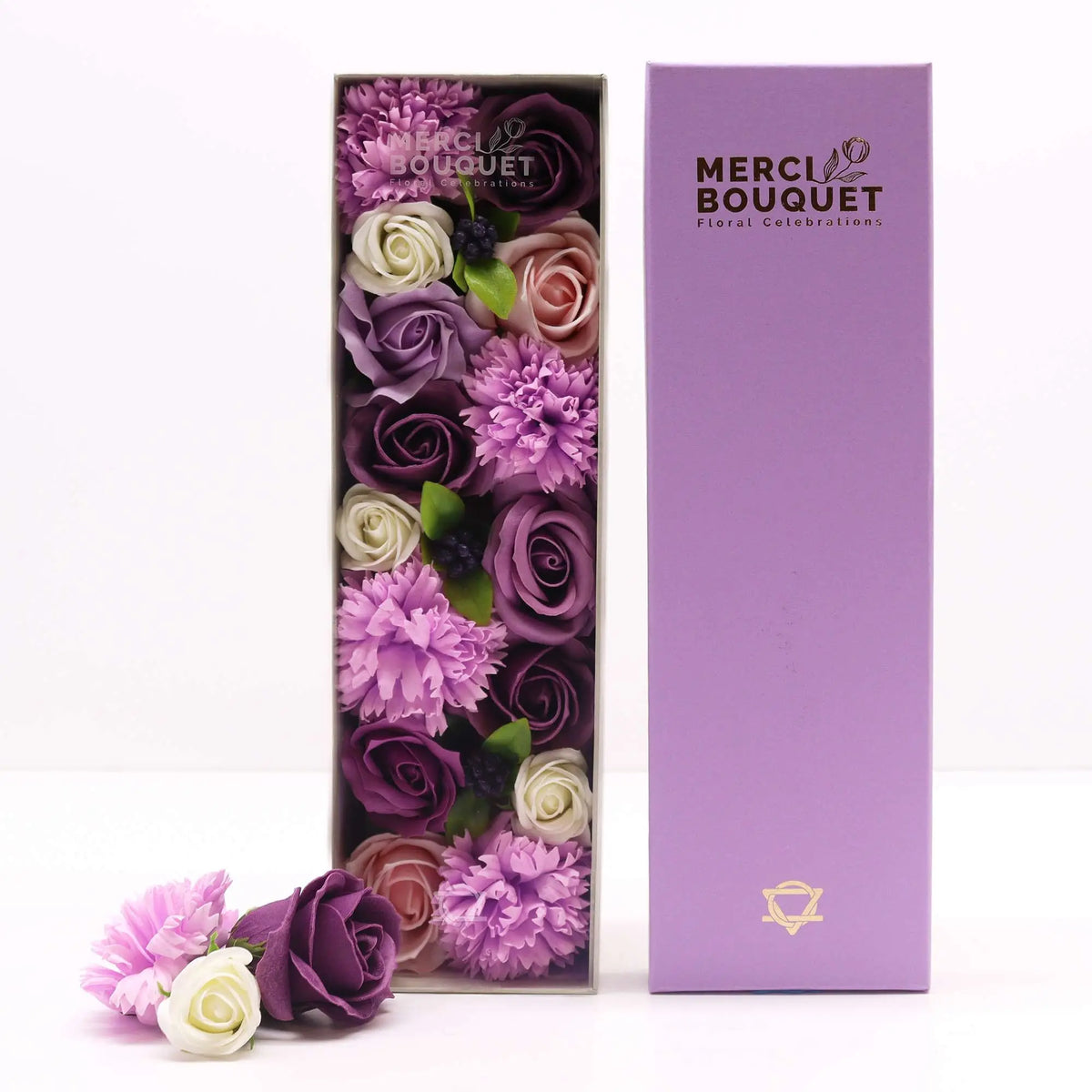Caja alargada con rosas y claveles de jabón en tonos morados, lilas y blancos, acompañada de su tapa violeta.