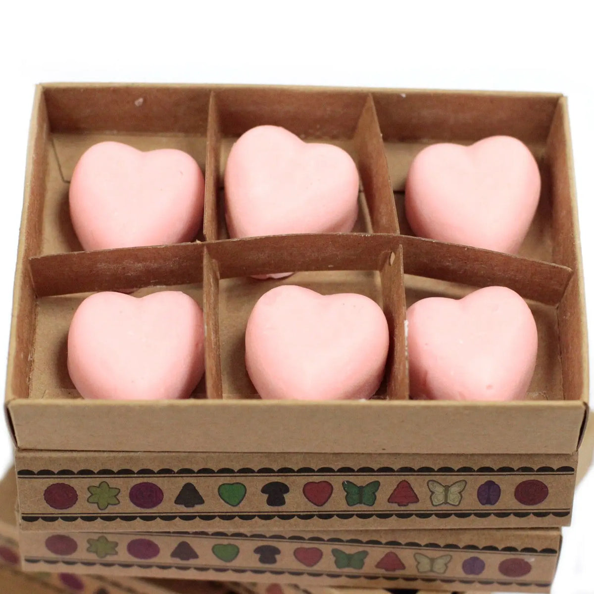 Caja de cartón con 6 ceras de soja en forma de corazón color rosa pálido, decorada con motivos geométricos y naturales.
