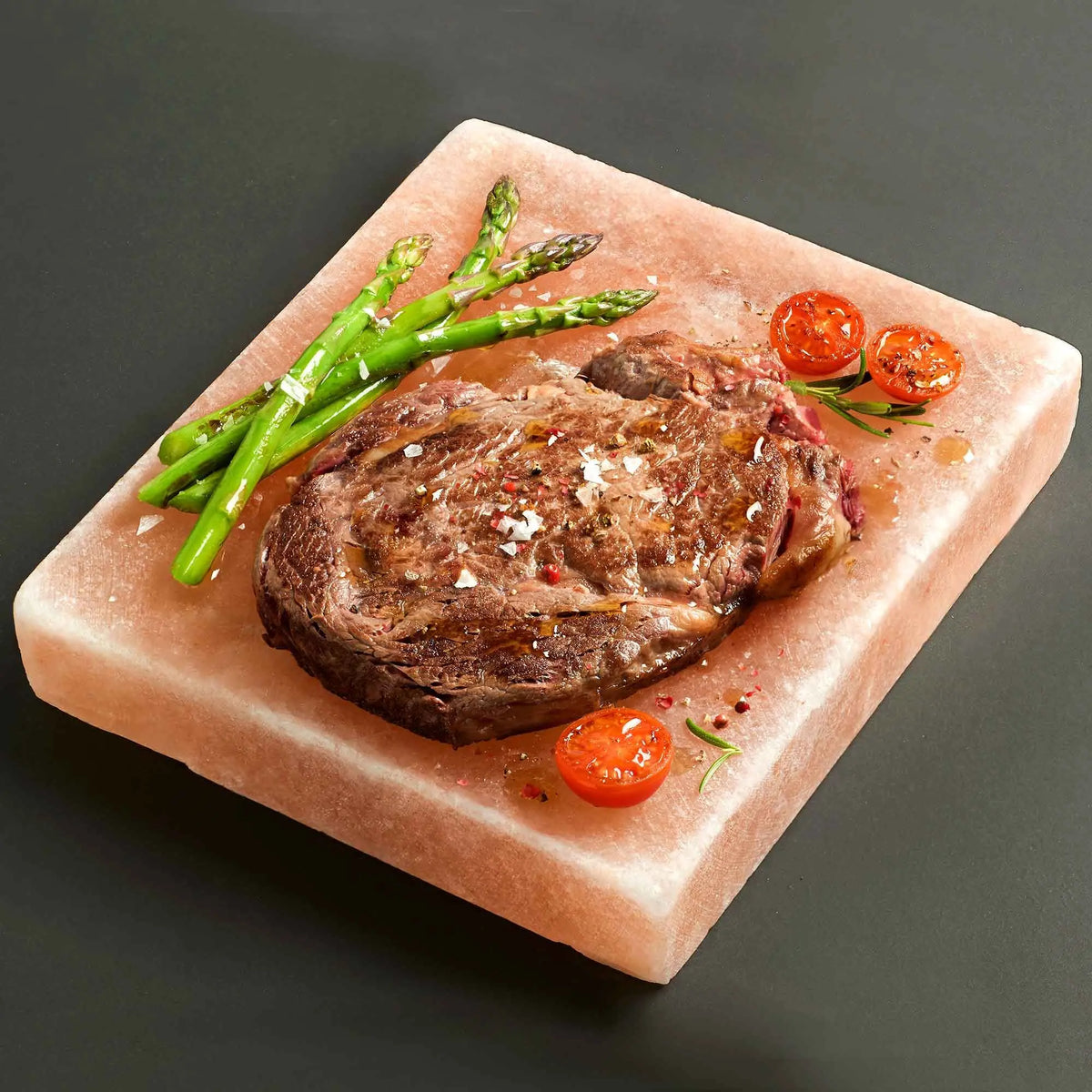 Plato cuadrado de sal rosa del Himalaya con filete, espárragos y tomates cherry sobre fondo oscuro.