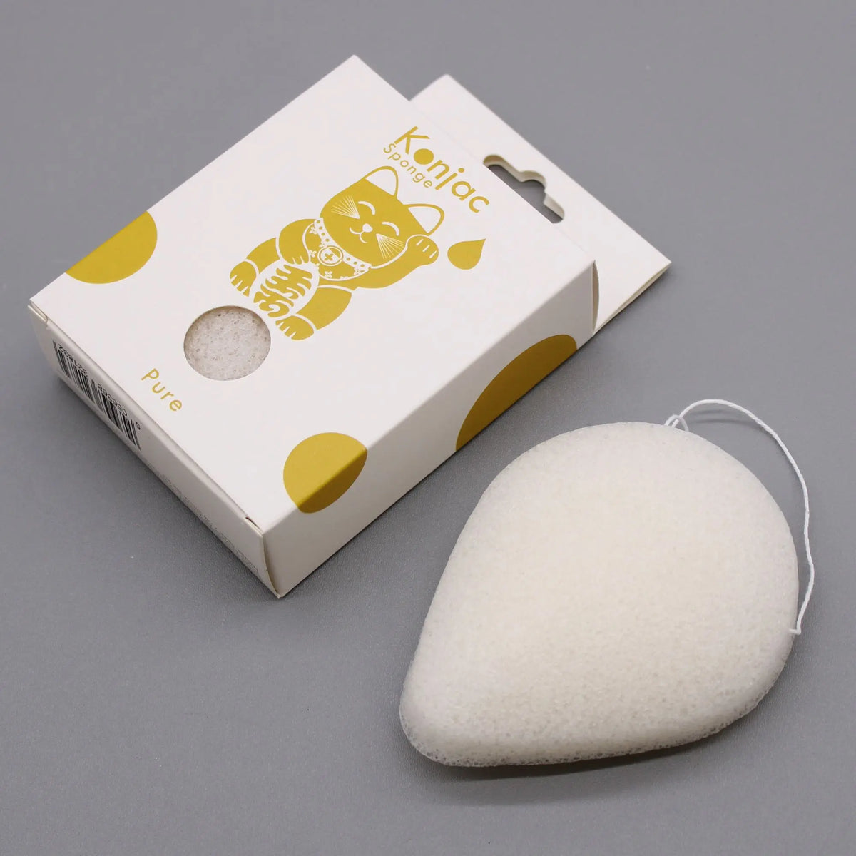 Esponja facial konjac blanca en forma de gota con cuerda, junto a su caja blanca con ilustraciones doradas.