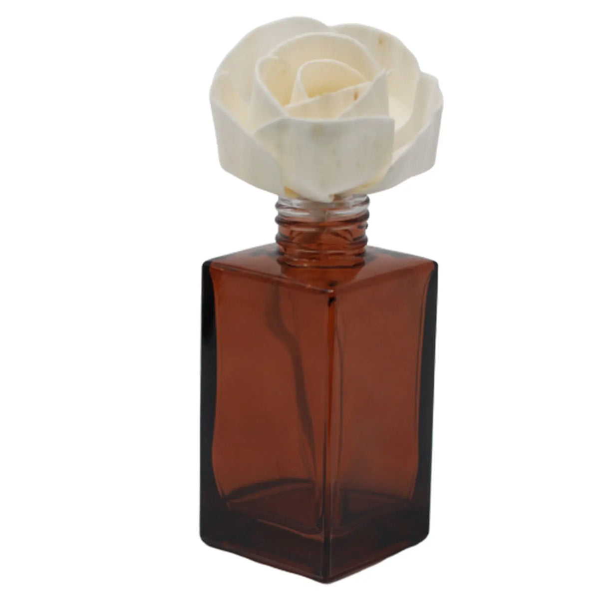 Rosa blanca de madera sobre frasco difusor de vidrio ámbar cuadrado con cuerda. Fondo blanco.