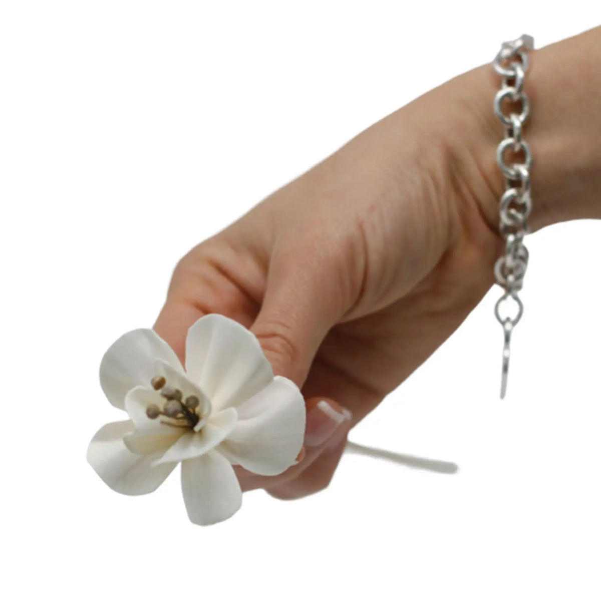 Mano sosteniendo una flor difusora blanca hecha de material natural con tallo de caña. Fondo blanco.