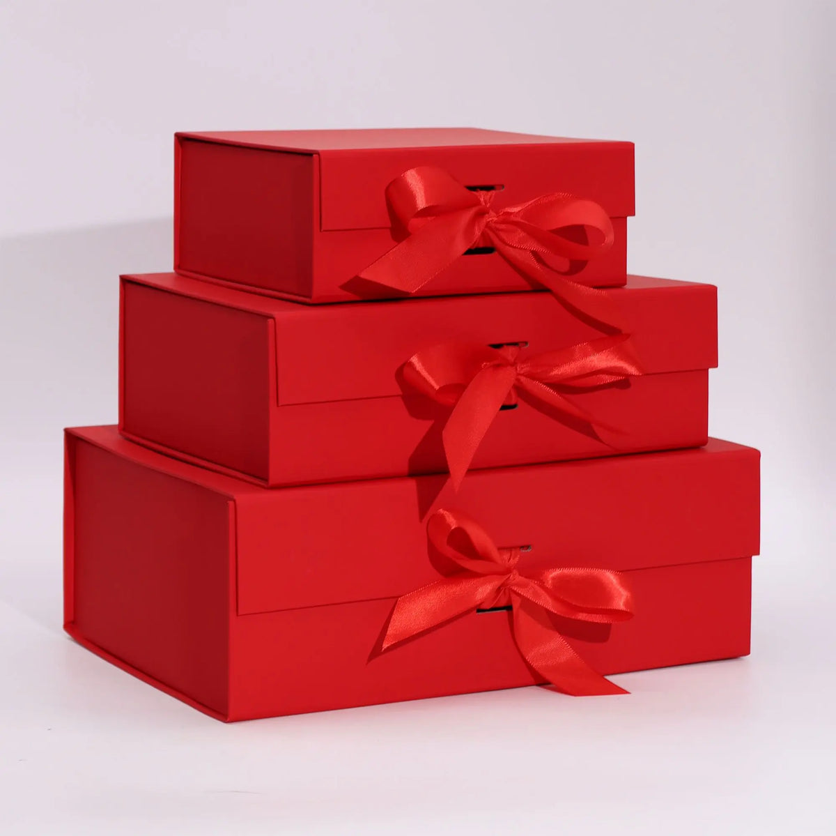 Torre de tres cajas de regalo rojas plegables, rectangulares y rígidas, decoradas con un lazo de cinta al frente.