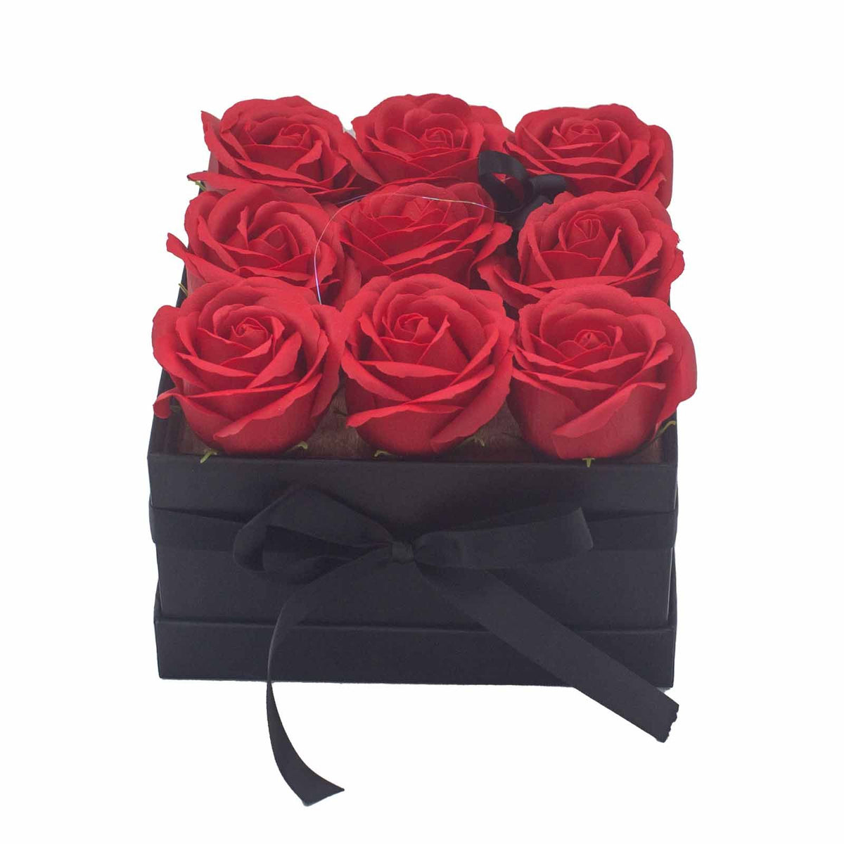 Caja cuadrada negra con lazo conteniendo 9 rosas rojas de jabón dispuestas en cuadrícula sobre fondo blanco.