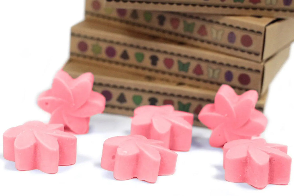Seis ceras de soja rosas con forma de flor frente a cajas de cartón kraft apiladas con un diseño decorativo geométrico