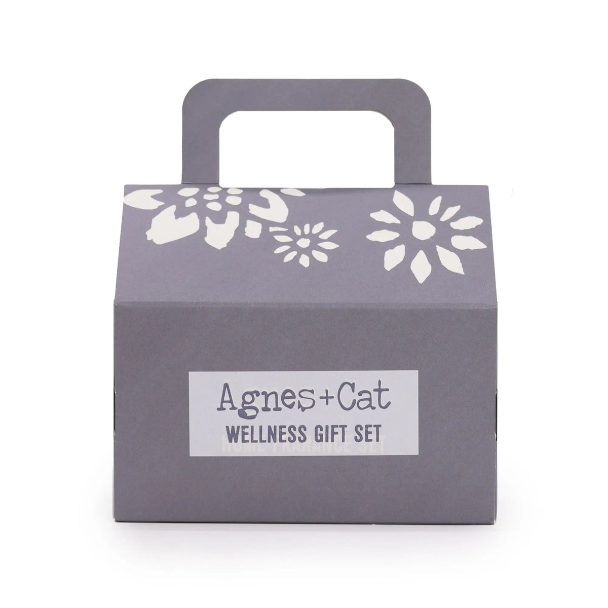 Caja de regalo gris con asa, detalles florales blancos y etiqueta central "Agnes + Cat Wellness Gift Set".