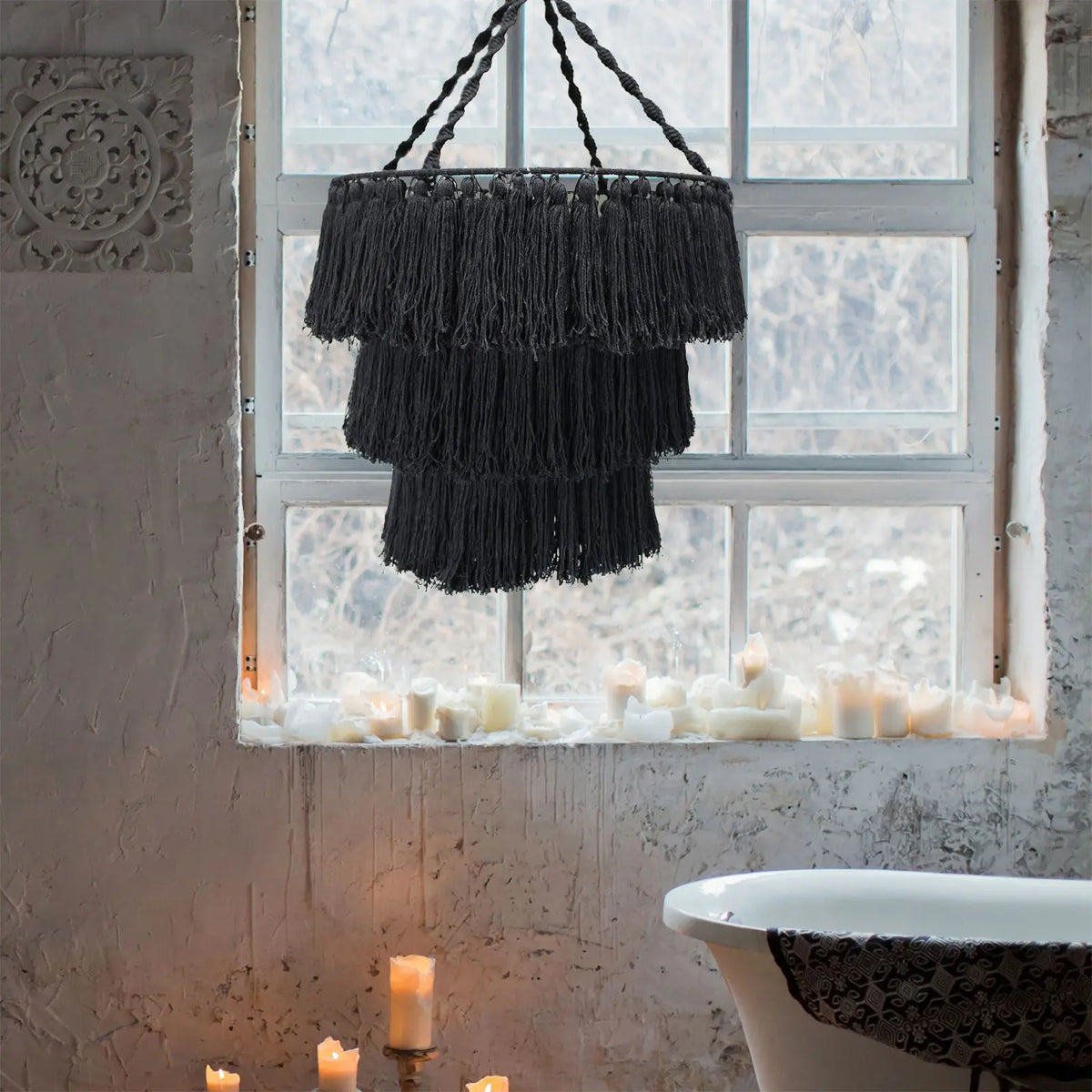 Lámpara de techo estilo araña en macramé negro, diseño de tres niveles con flecos, colgando frente a una ventana.