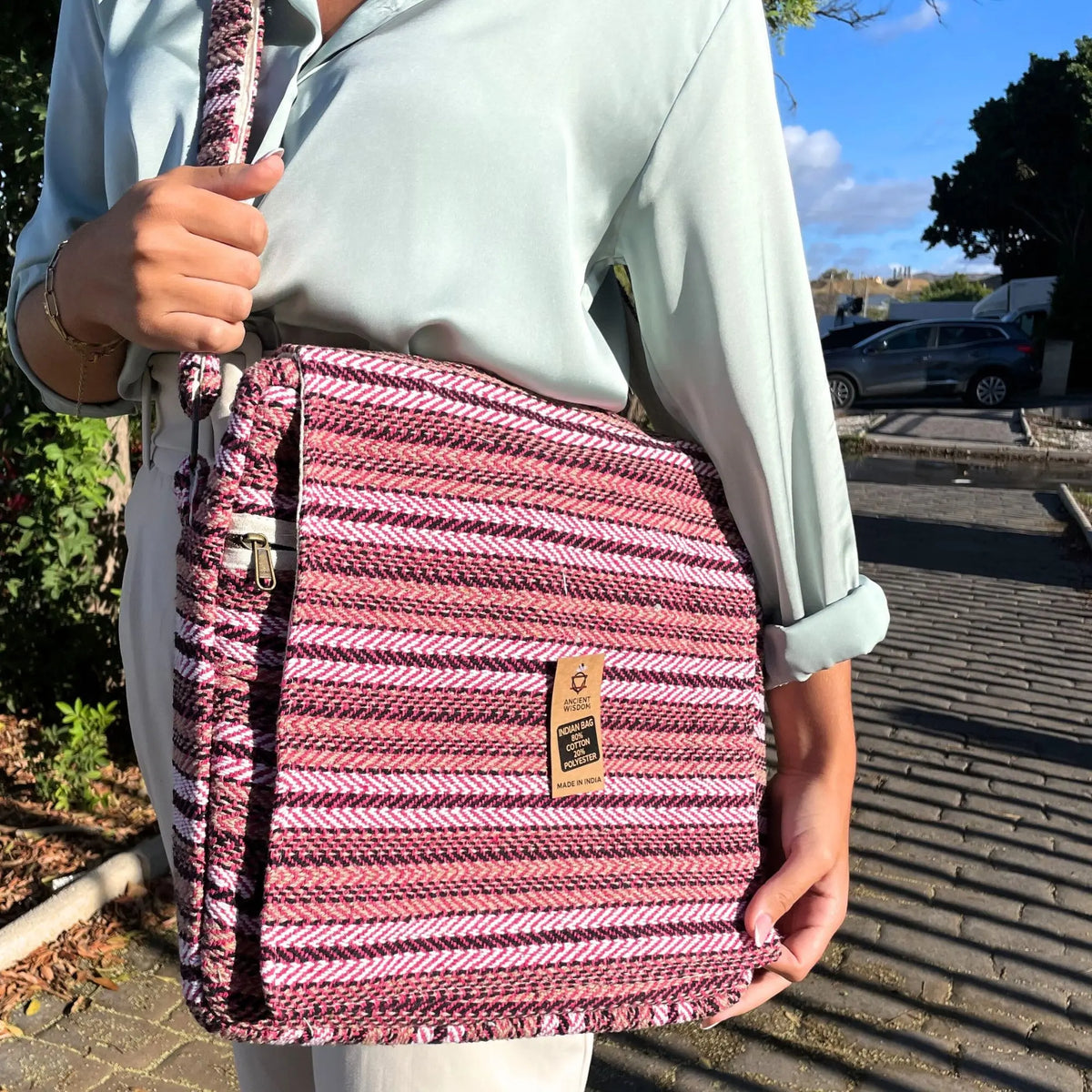 Bolso bandolera para portátil con tejido de rayas horizontales en tonos rosa, blanco y negro y correa a juego.