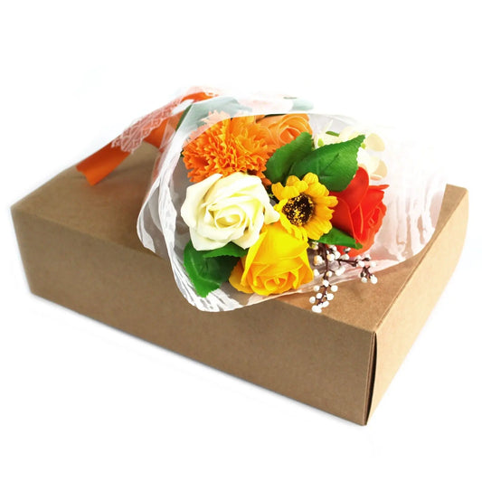 Bouquet de flores de jabón en tonos naranja y amarillo sobre una caja de cartón rectangular, envuelto para regalo.