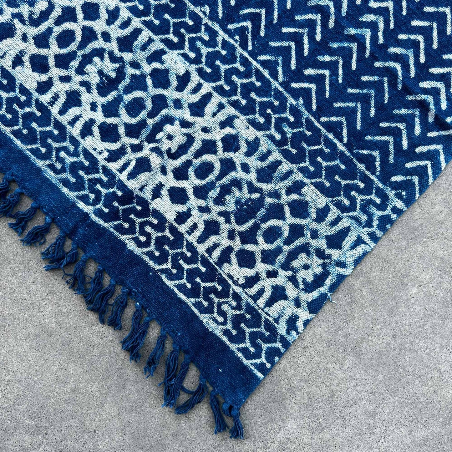 Alfombra azul marino de algodón, con diseño geométrico en tonos claros y flecos decorativos.