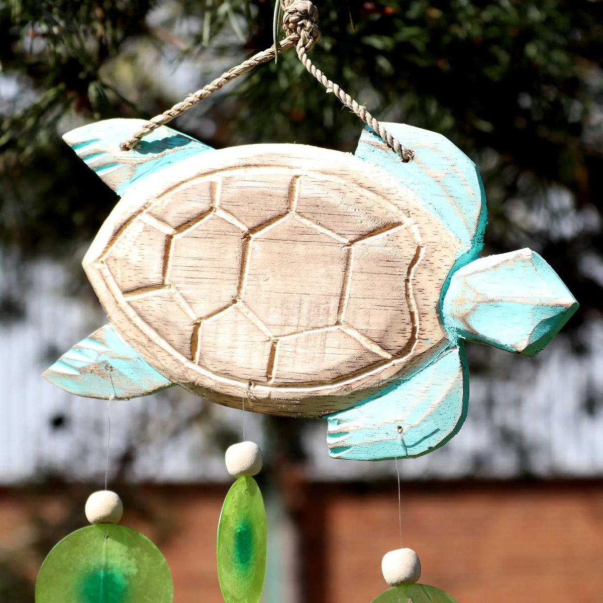 Carillón de madera tallada en forma de tortuga color turquesa con colgantes de gotas verdes y cuentas de madera.