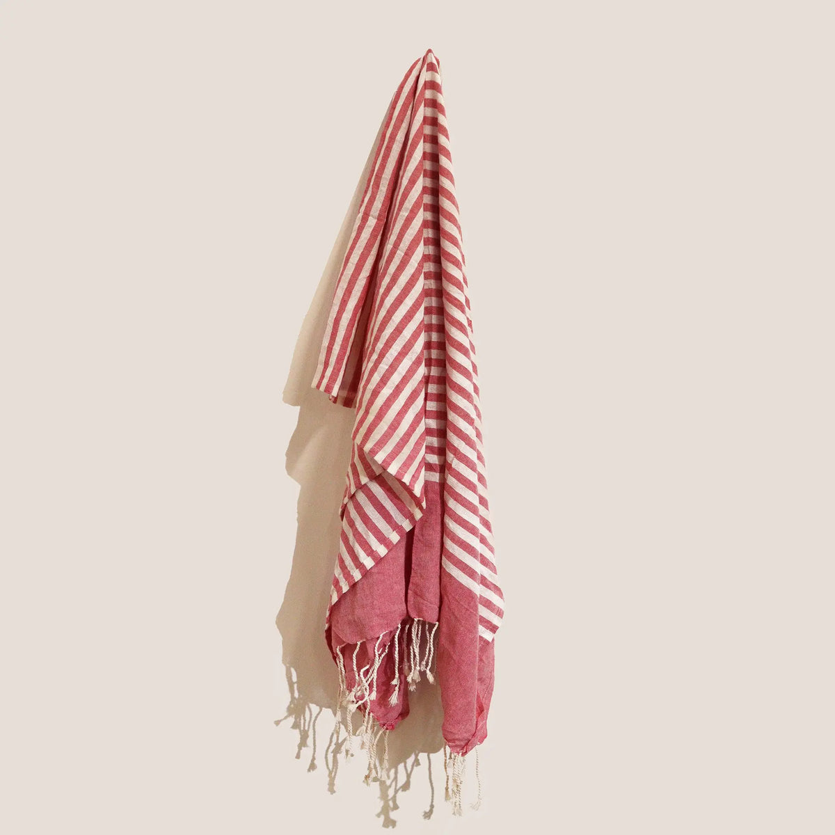 Pareo de algodón artesanal a rayas color rosa intenso y crema, con flecos en los extremos, colgado verticalmente.