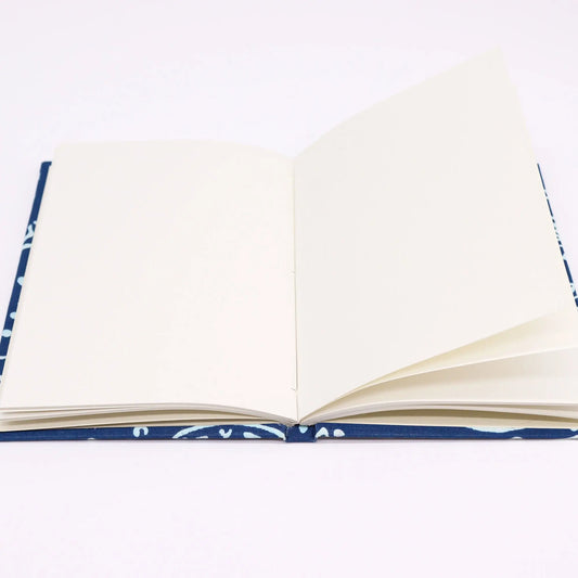 Cuaderno abierto con hojas blancas y tapa de tela azul marino con estampado de peces blancos sobre fondo claro.