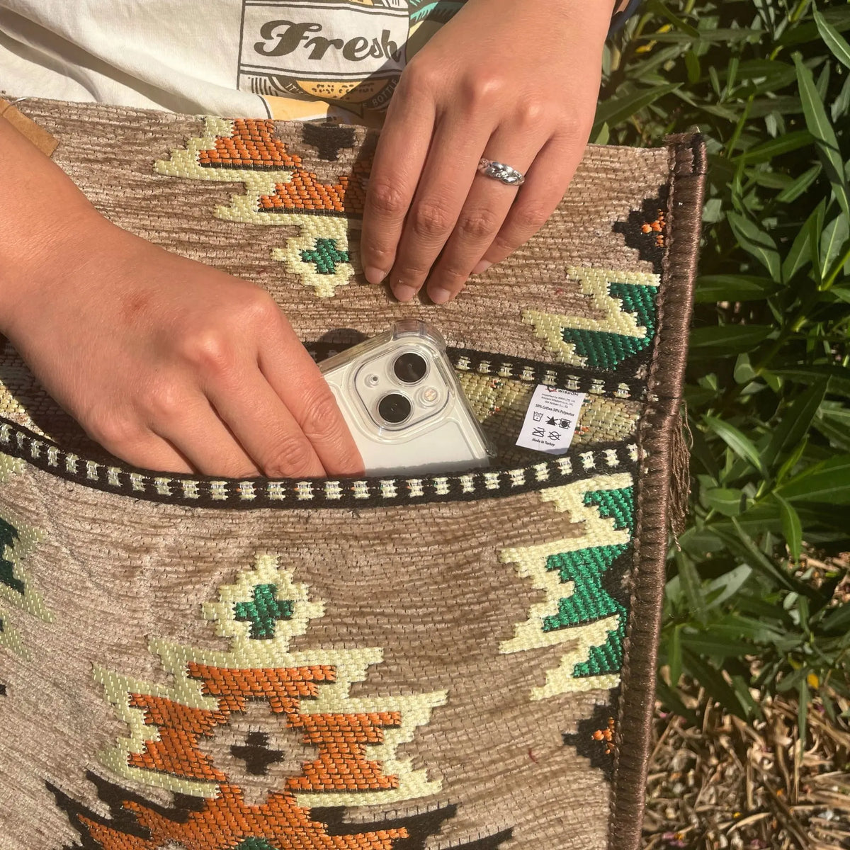 Bolso bandolera de estilo kilim beige con tejido texturizado y patrones geométricos en tonos naranjas y verdes