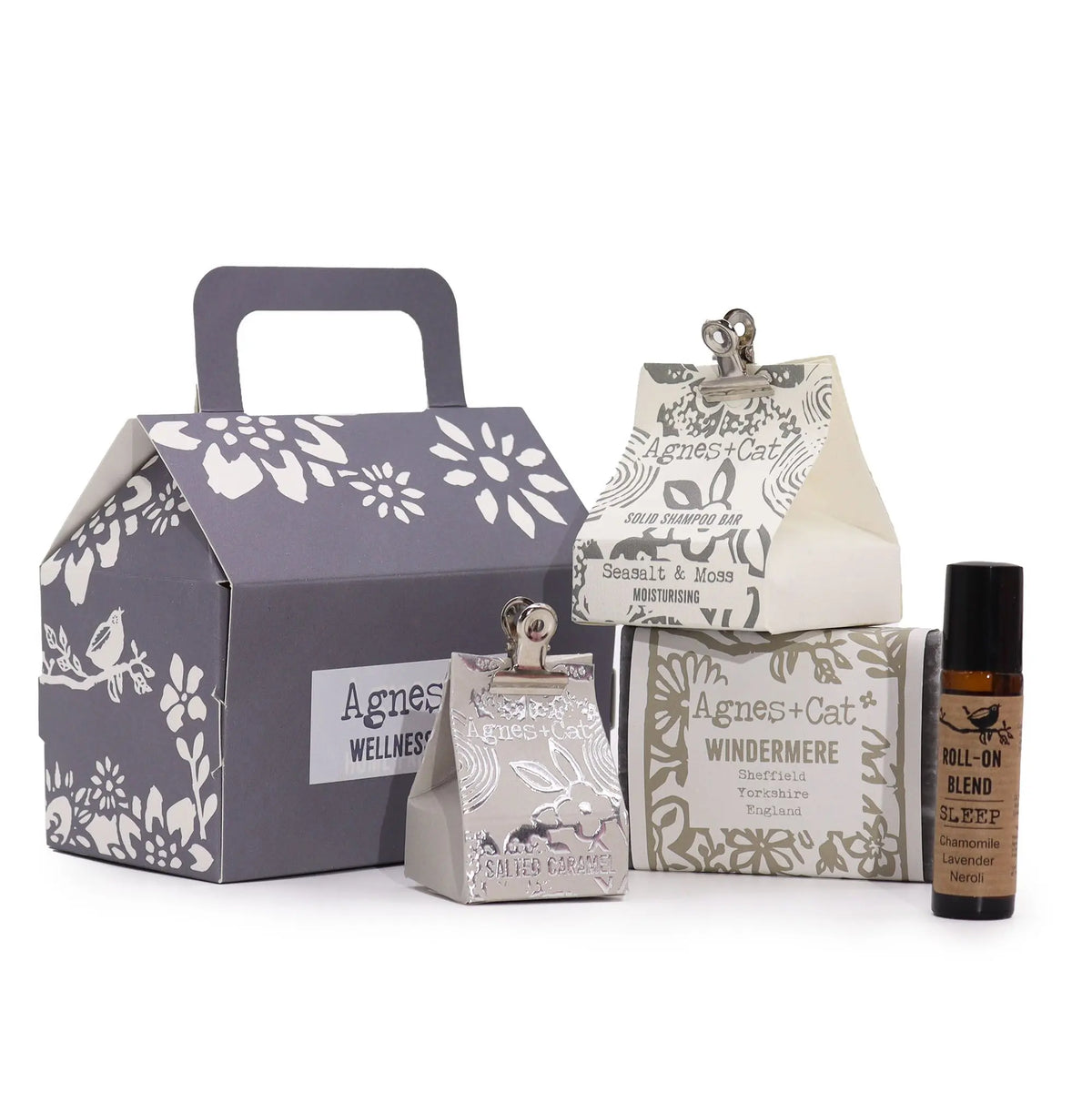 Conjunto de bienestar Agnes & Cat: caja gris, champú sólido, jabón Windermere y roll-on de aromaterapia sobre fondo blanco.
