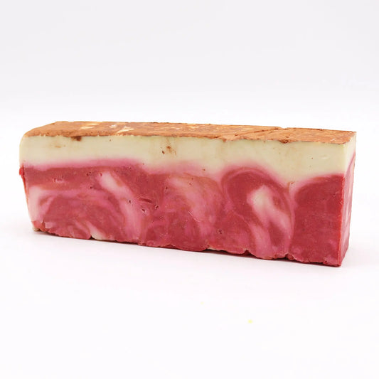 Barra de jabón artesanal rectangular con franjas de color crema y tonos rojizos jaspeados sobre fondo blanco.