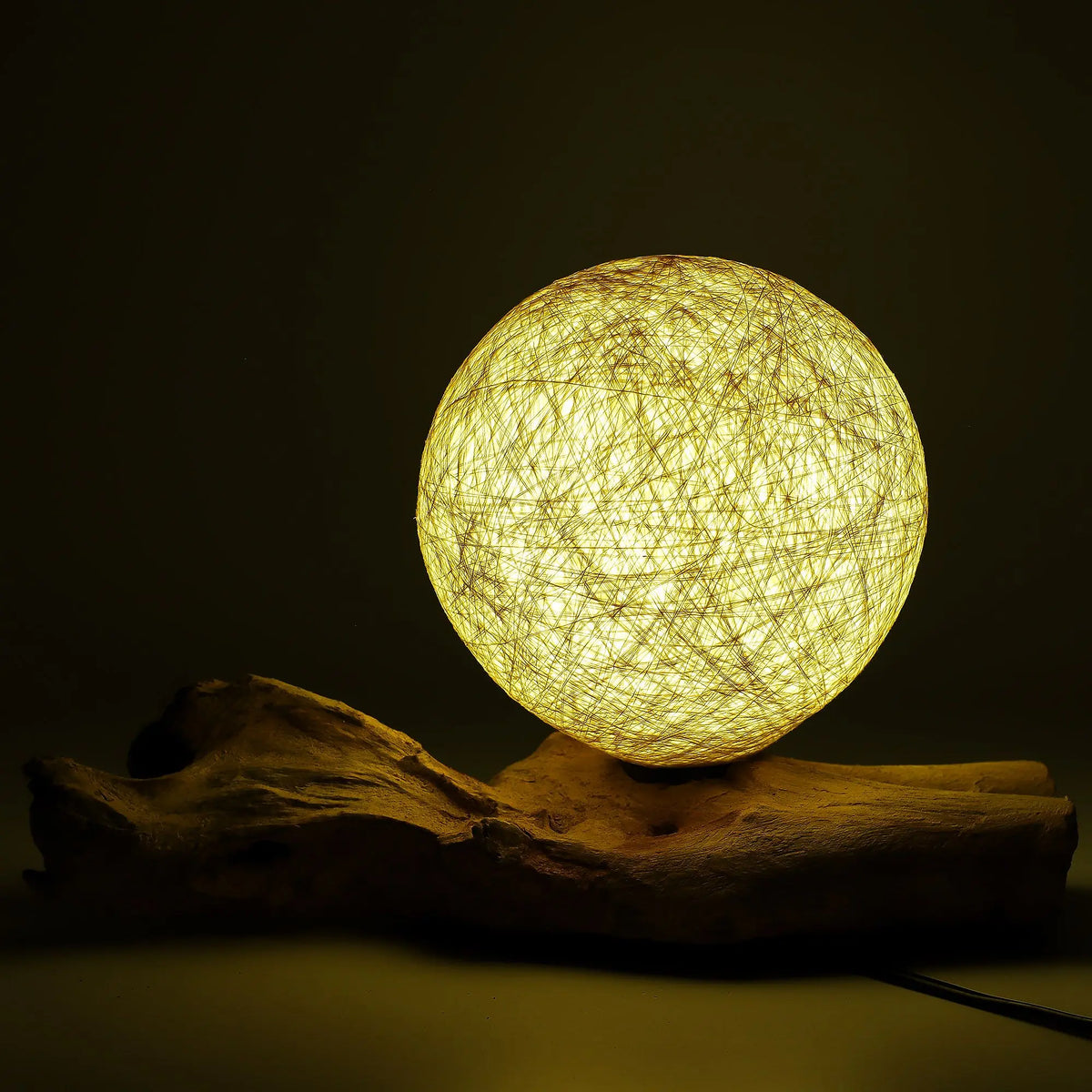 Lámpara de mesa con esfera de hilo color crema sobre una base de madera rústica que emite una luz cálida y difusa.