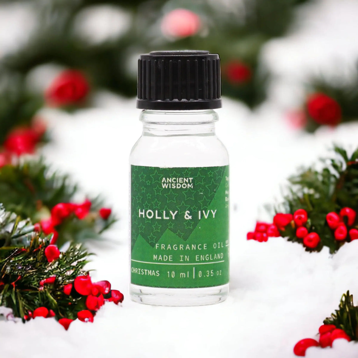 Frasco de 10ml de aceite con etiqueta verde sobre nieve, rodeado de ramas de acebo con frutos rojos.