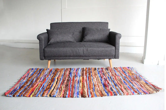 Alfombra rectangular de trapo india, 105x185cm, con tiras multicolores tejidas en franjas. Estilo artesanal y rústico.