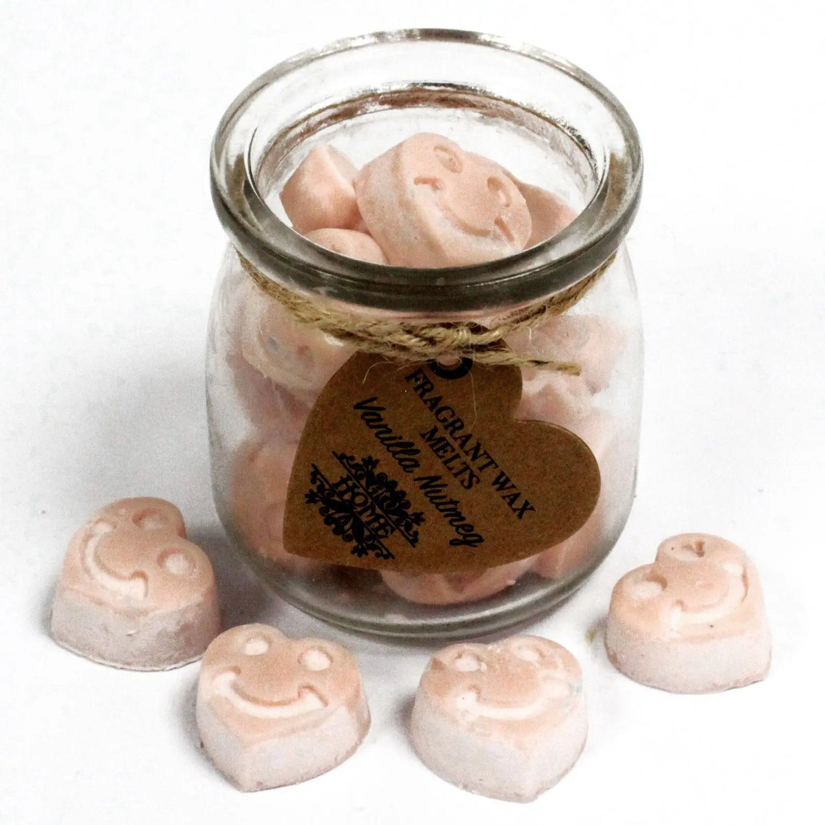 Frasco de vidrio lleno de pastillas de cera de soja color crema con caras sonrientes, con etiqueta de corazón y cordel.