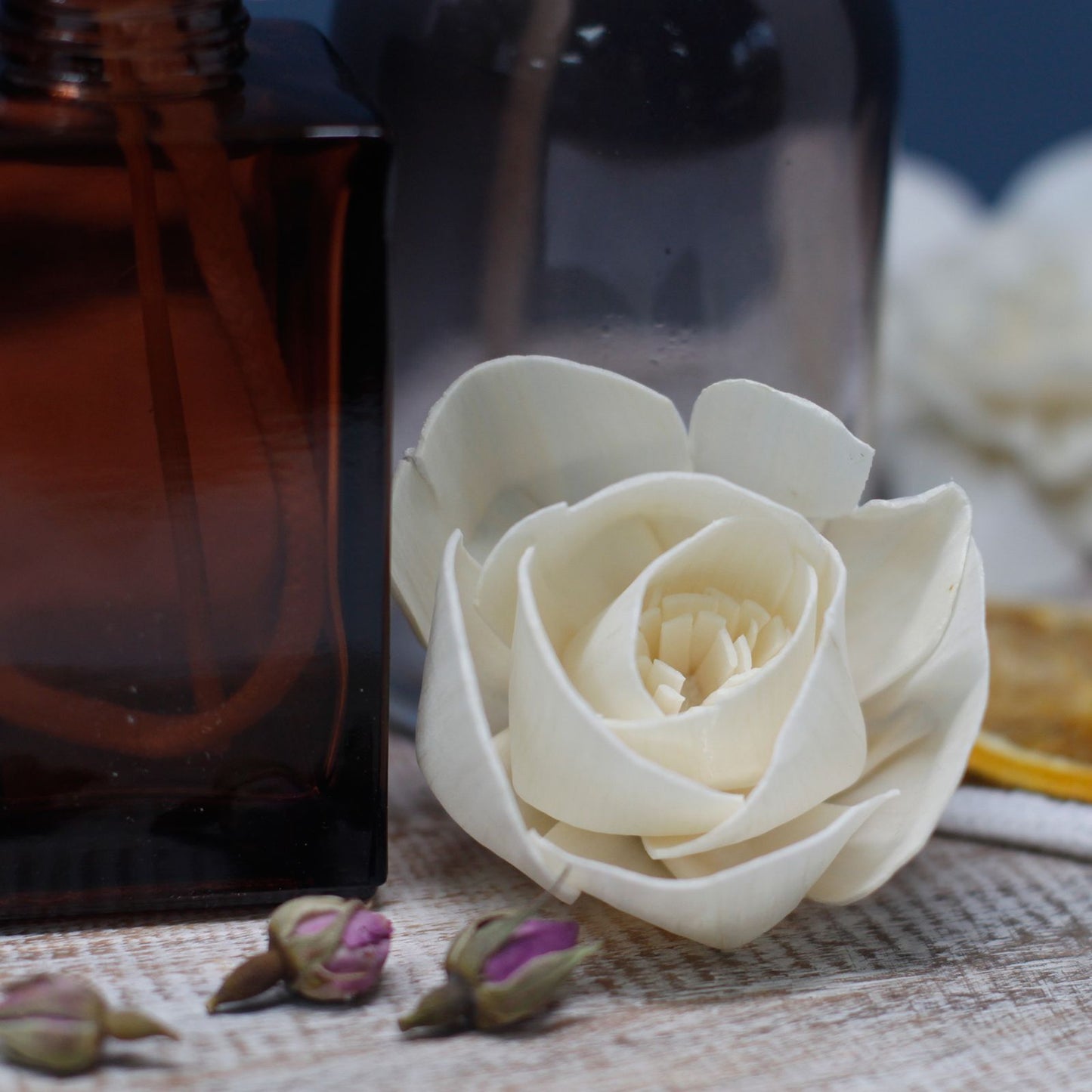 Flor difusora blanca de madera sobre mesa de madera, junto a frasco de vidrio ámbar. Estilo natural y minimalista.