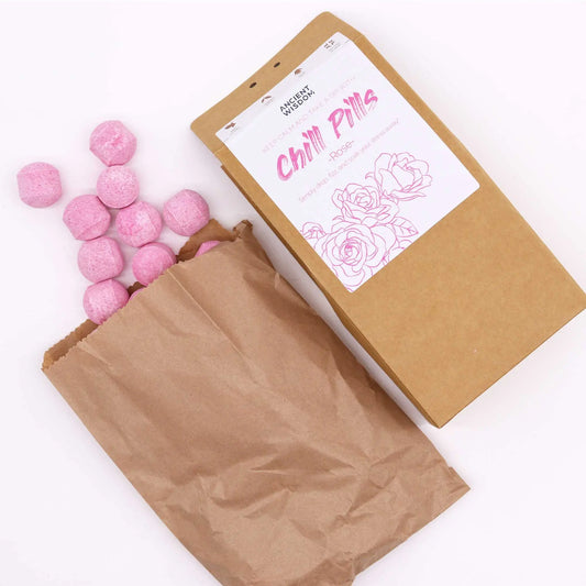 Bolsa de papel kraft con mini bombas de baño efervescentes de color rosa con aroma a rosas sobre fondo blanco.