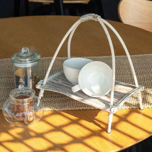 Soporte blanco de hoja de coco con asa, estilo artesanal, exhibiendo dos tazas blancas sobre mesa de madera