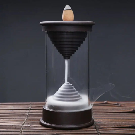 Quemador de incienso de flujo inverso, con diseño tubular de vidrio, base de madera y humo descendente en espiral.