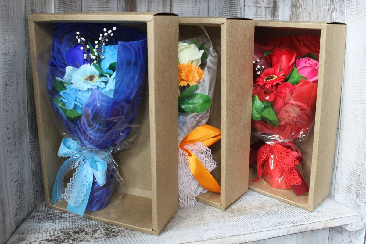 Tres ramos de flores de jabón de colores azul, naranja y rojo, presentados en cajas de cartón individuales.