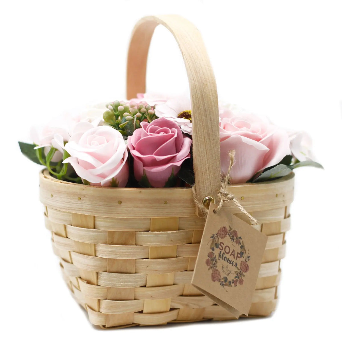 Cesta de mimbre con asa llena de flores de jabón en tonos rosa, con etiqueta colgante sobre fondo blanco.