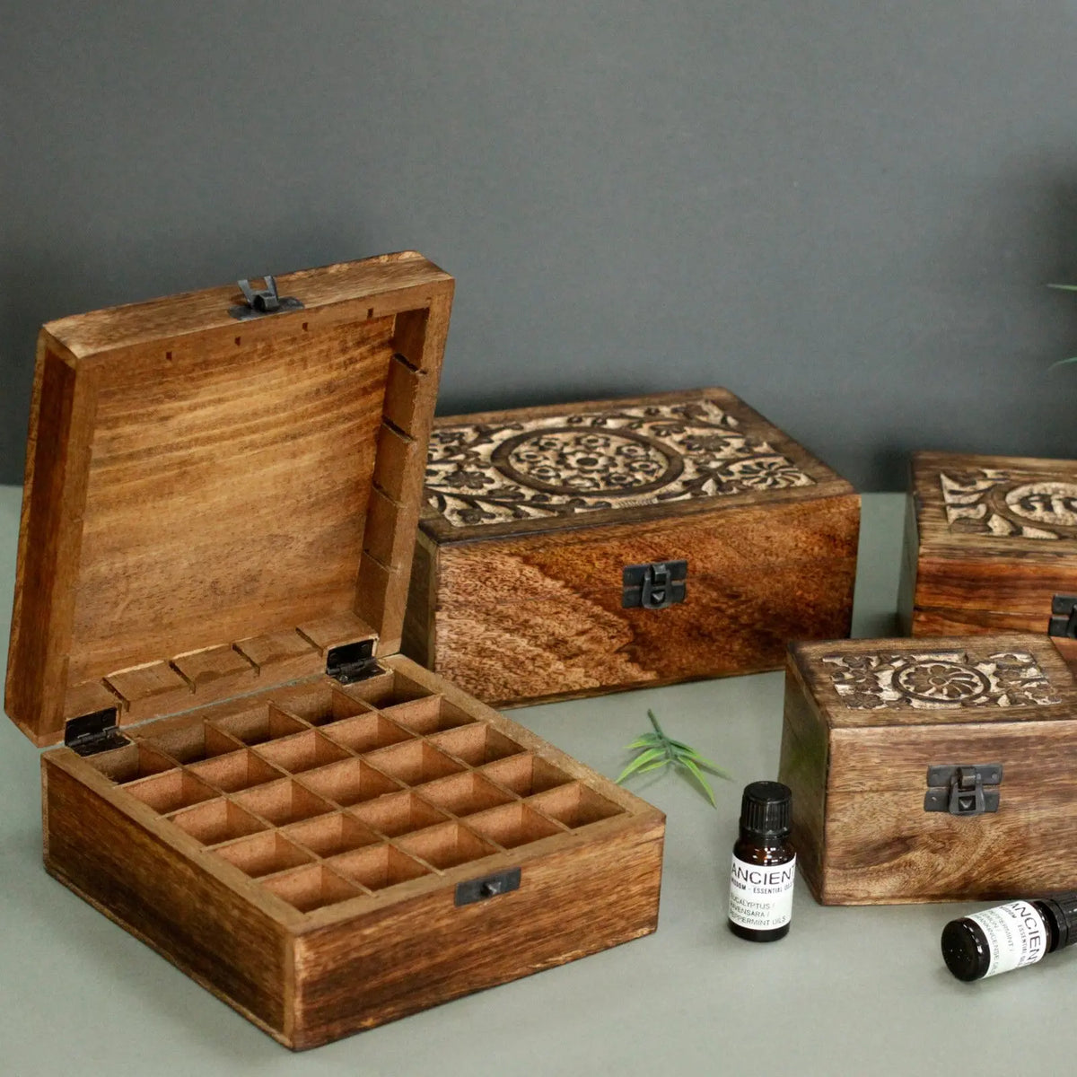 Caja de madera de mango con compartimentos para 25 aceites esenciales y tapa decorada con motivos florales tallados.