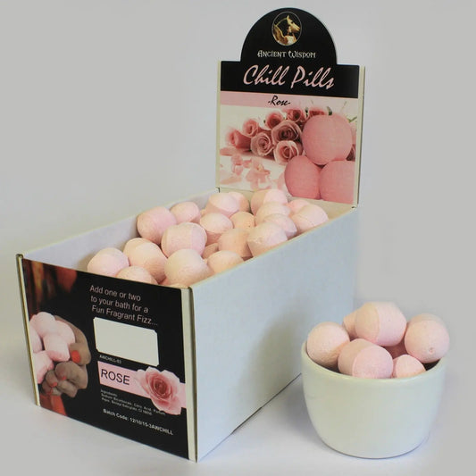 Caja de exhibición con mini bombas de baño efervescentes de color rosa y aroma a rosas, junto a un cuenco lleno.