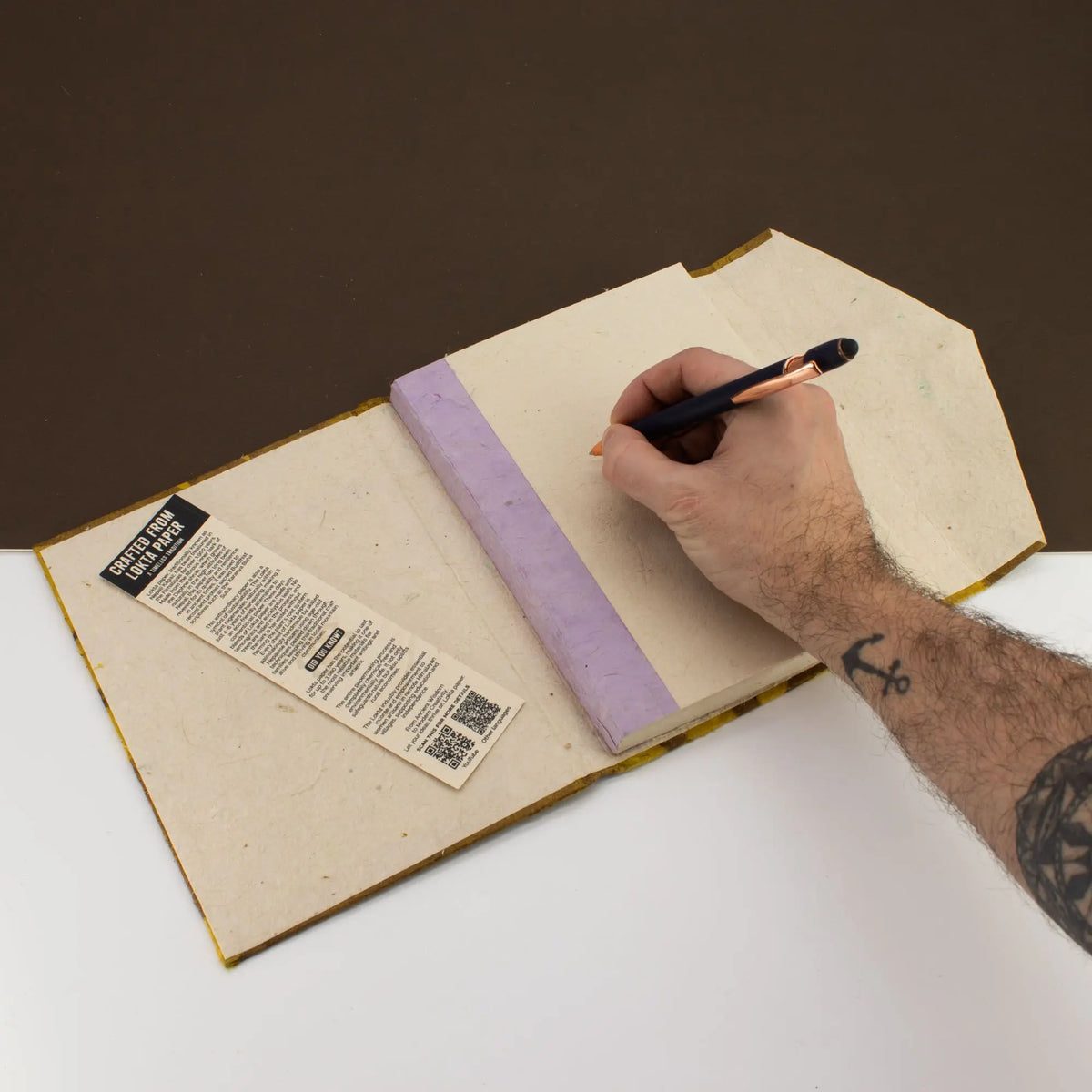 Cuaderno ecológico de papel reciclado, tapa color lavanda, con pluma negra, estilo minimalista.
