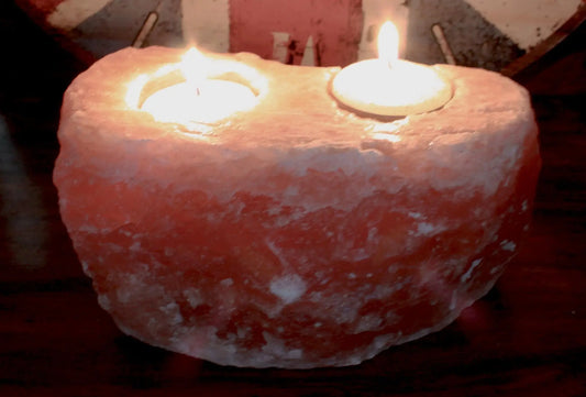 Portavelas de sal del Himalaya rosa con dos huecos circulares y velas encendidas, de textura rugosa y acabado natural.