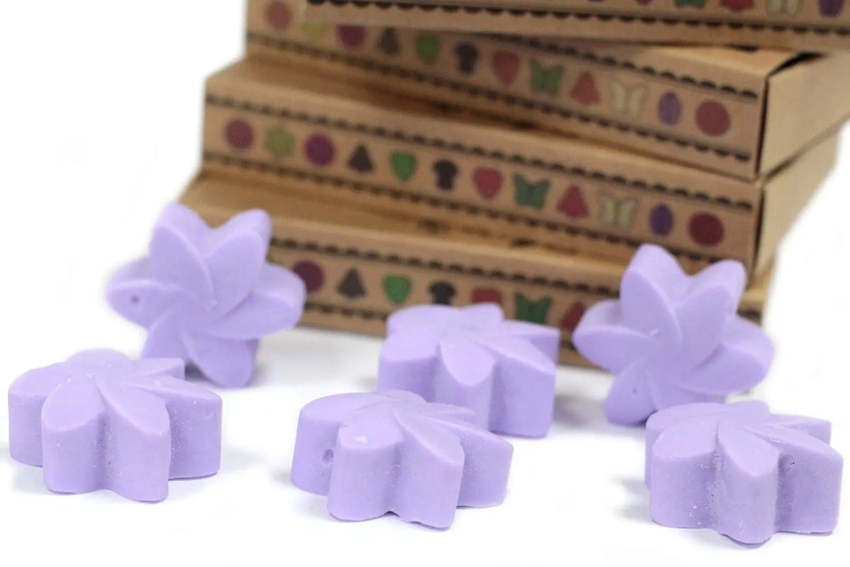 Seis ceras de soja en forma de flor color lavanda frente a una pila de cajas de regalo de cartón kraft.