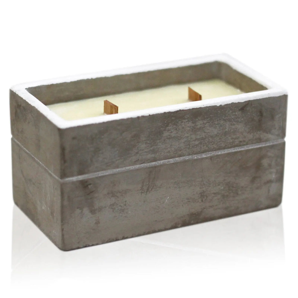 Vela rectangular de hormigón gris con dos mechas de madera, sobre fondo blanco y superficie con reflejo.