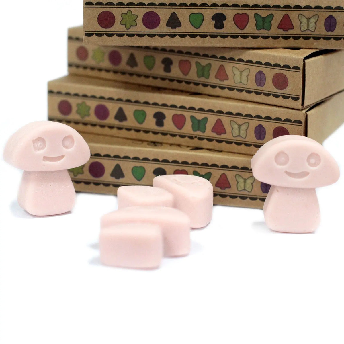 Cajas de cartón kraft con iconos y ceras de soja rosas con forma de champiñones sonrientes frente a ellas.