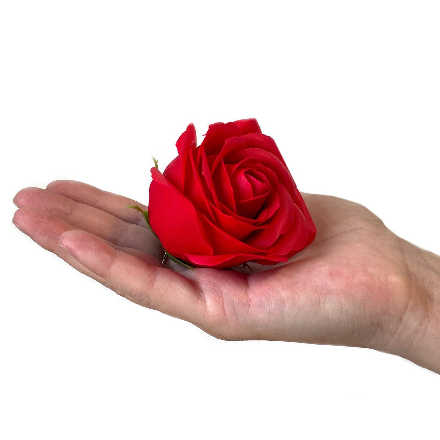 Mano abierta sosteniendo una rosa roja de jabón con pétalos realistas sobre un fondo blanco.