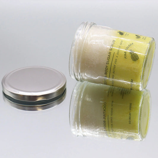 Frasco de vidrio con exfoliante de azúcar amarillo y tapa metálica plateada sobre fondo blanco.