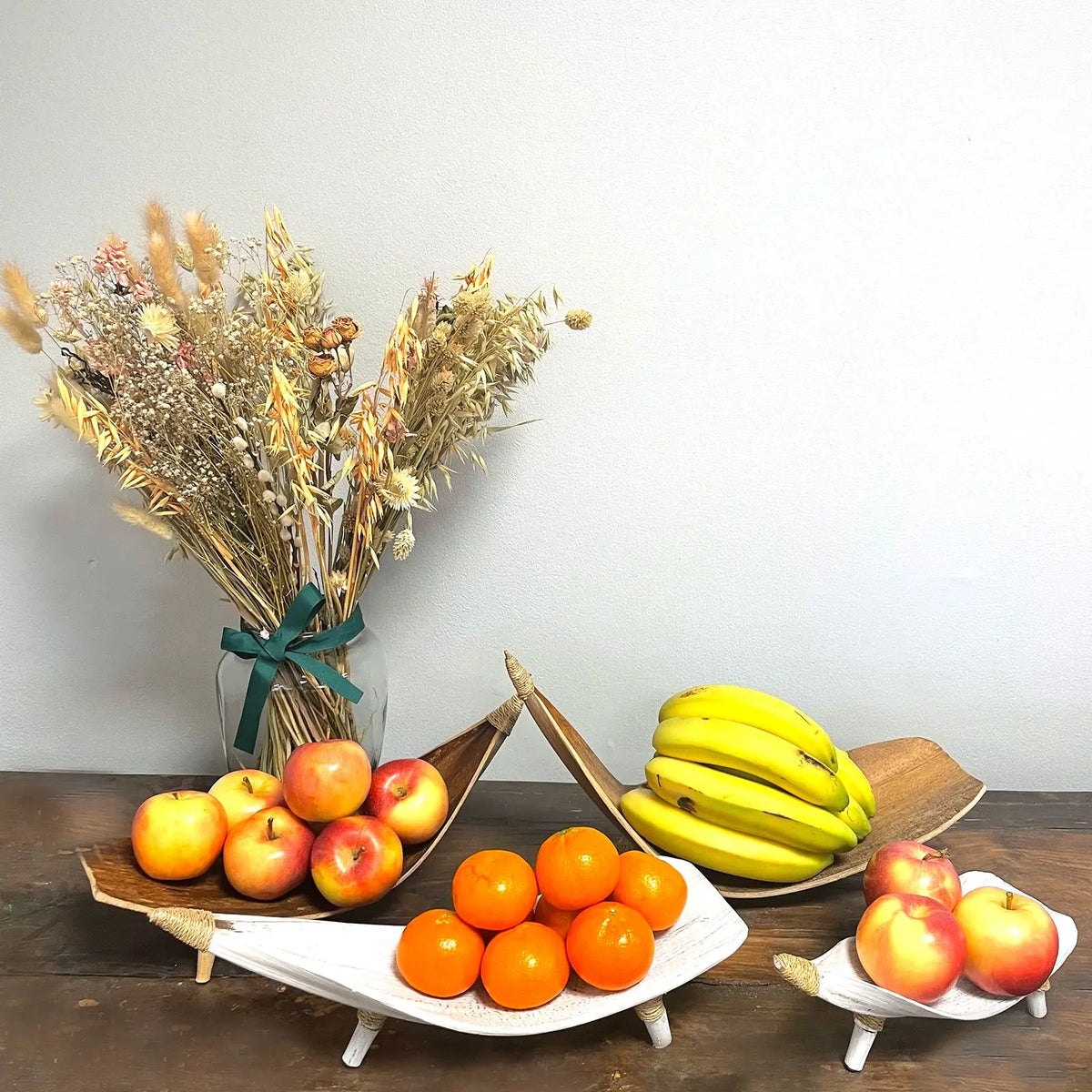 Fruteros artesanales de hoja de coco en blanco y natural con frutas frescas sobre una mesa de madera.