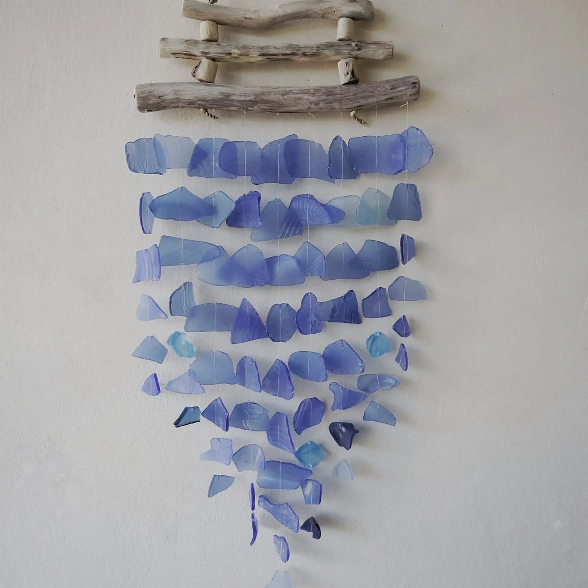 Carrillón decorativo de piezas de vidrio azul traslúcido suspendidas de tres ramas de madera natural.