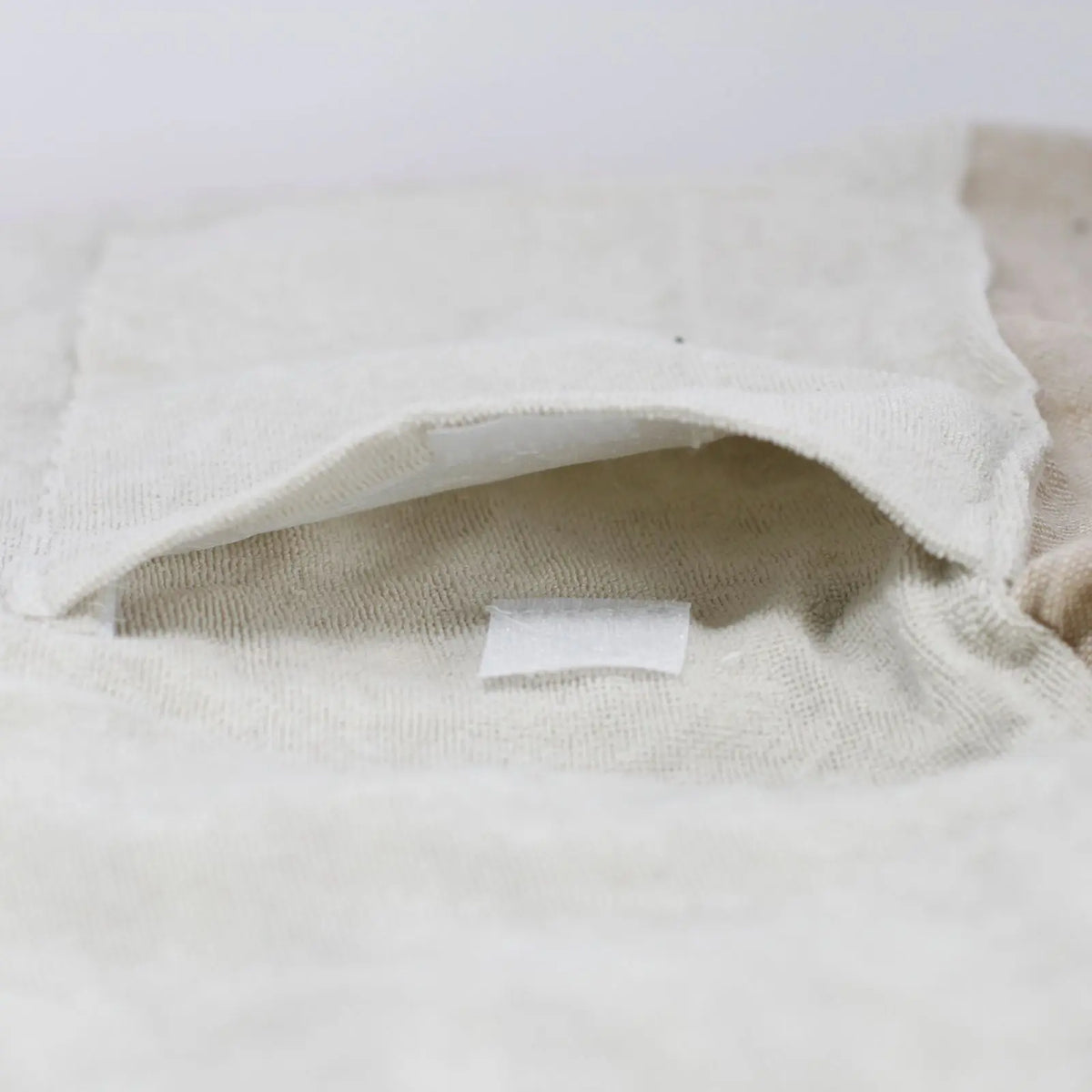 Detalle en primer plano de bolsillo de toalla pareo de algodón color arena, con cierre de velcro en textura suave.