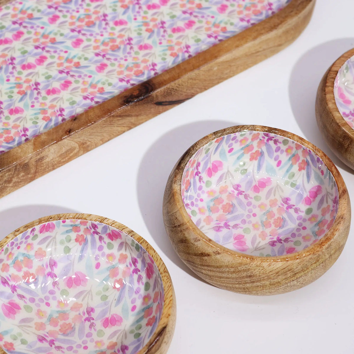 Bandeja y cuencos de madera de mango con estampado floral en tonos rosa y lila sobre fondo blanco.