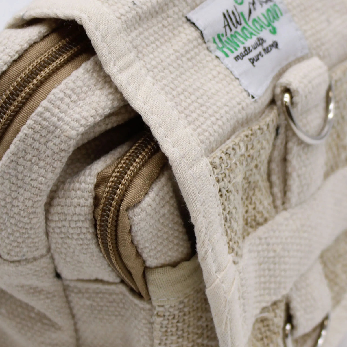 Primer plano de bolsa cruzada de cáñamo beige con textura natural, cremalleras marrones y herrajes metálicos.