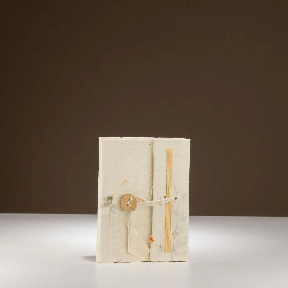 Cuaderno artesanal de papel reciclado en color blanco, cerrado con un botón de madera y atado con cuerda natural.