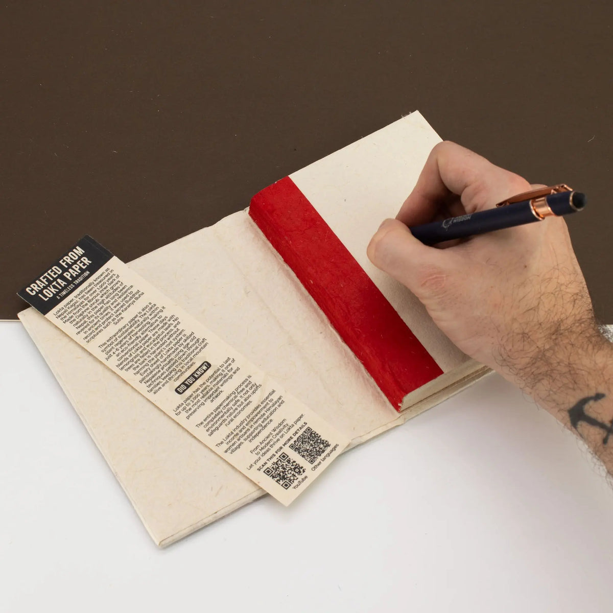 Cuaderno artesanal de papel reciclado con borde rojo y etiqueta negra, perfecto para escribir y tomar notas.